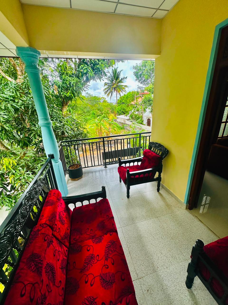 Covered balcony with traditional red-cushioned seating and a view of palms and mango trees