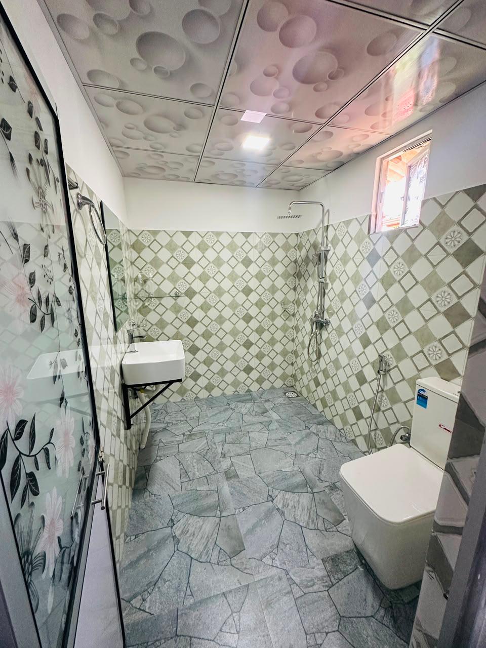 Clean tiled bathroom with rain shower, basin and toilet