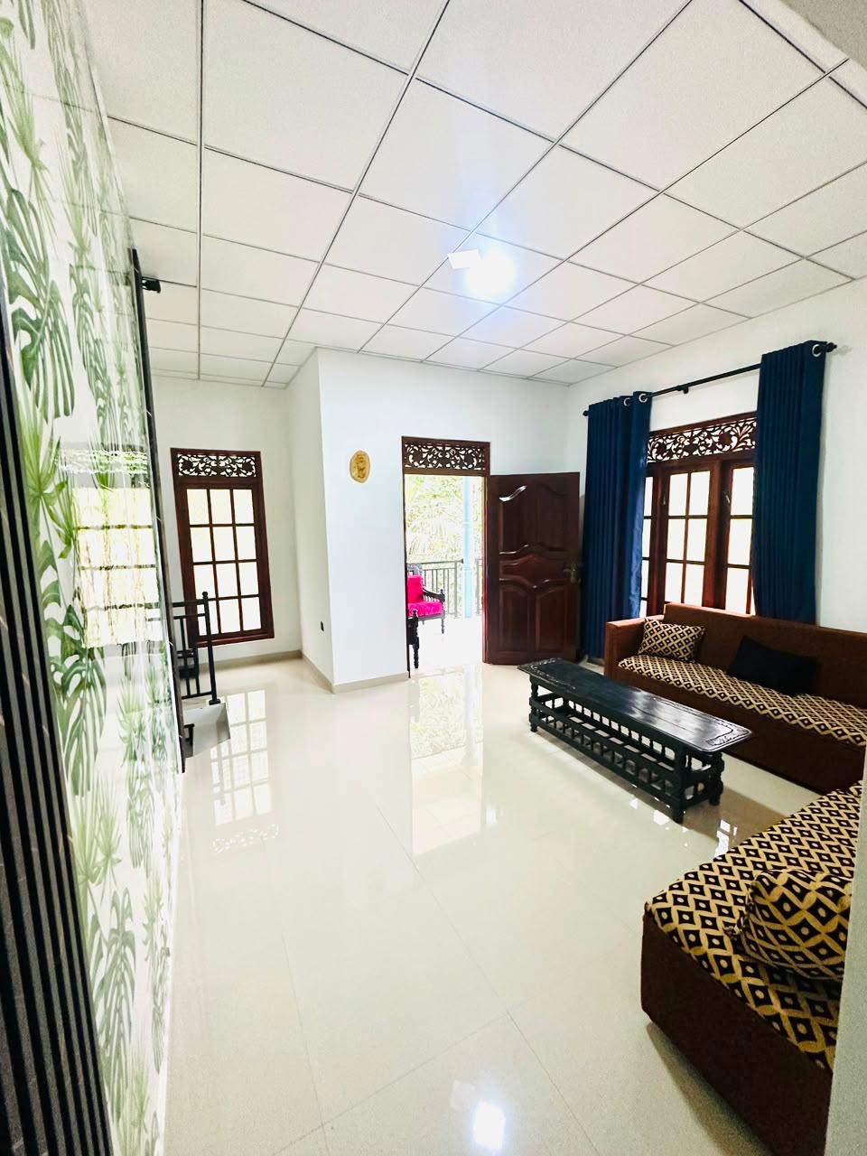 Spacious tiled guest lounge at Silva Homestay with sofas, a dark wooden coffee table, navy curtains and doors to the balcony