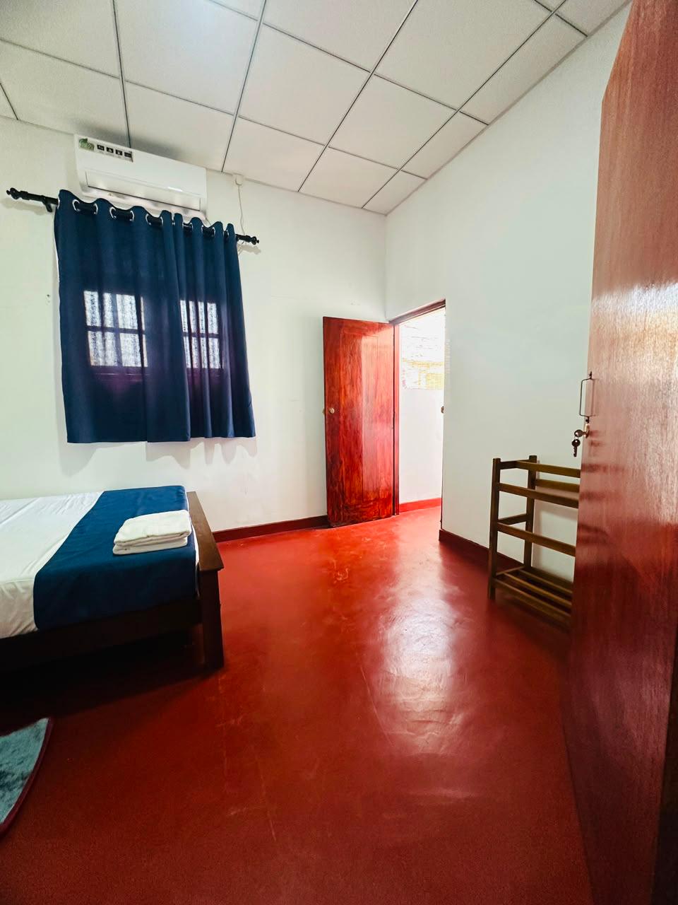 Guest room with A/C unit, navy curtains, bed with fresh towels and a wooden shoe rack