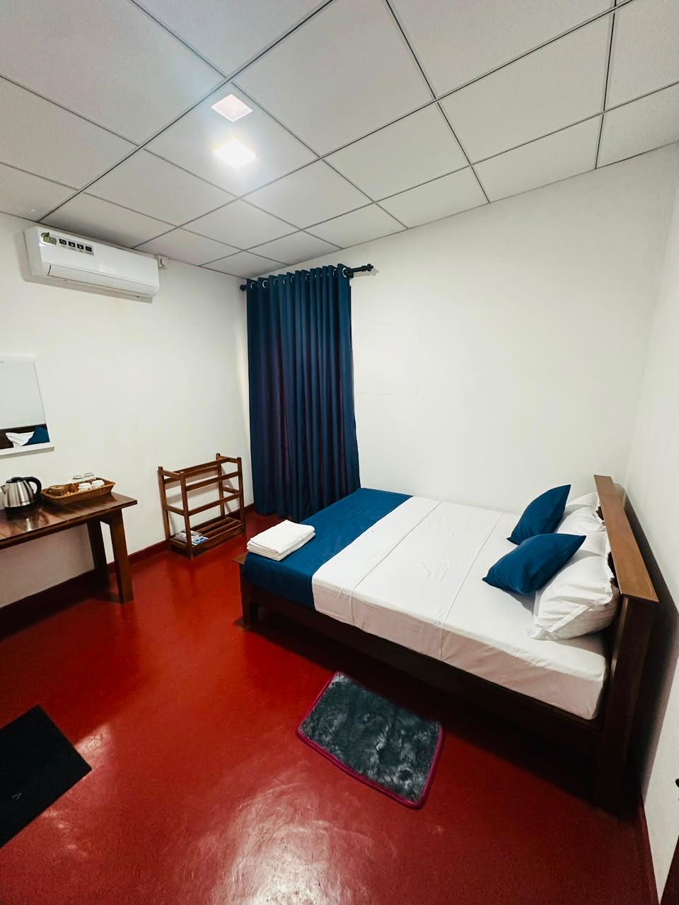 Air-conditioned guest room with a double bed, blue cushions and fresh towels, a desk with kettle and tea tray, and navy curtains